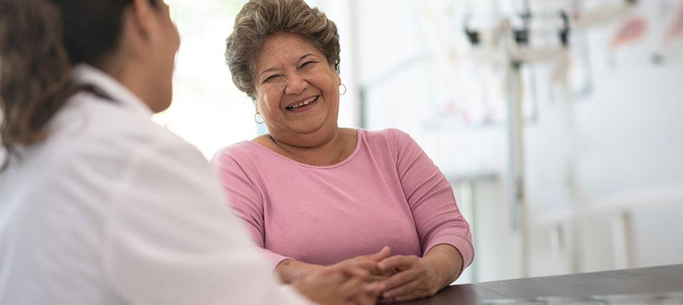 A person smiling at another in a white coat in a medical setting.