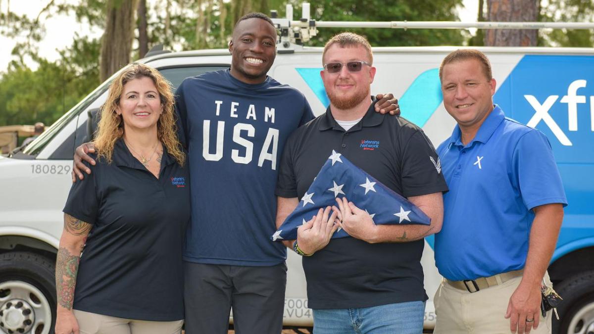 Four people posed together, one holding a folded flag.