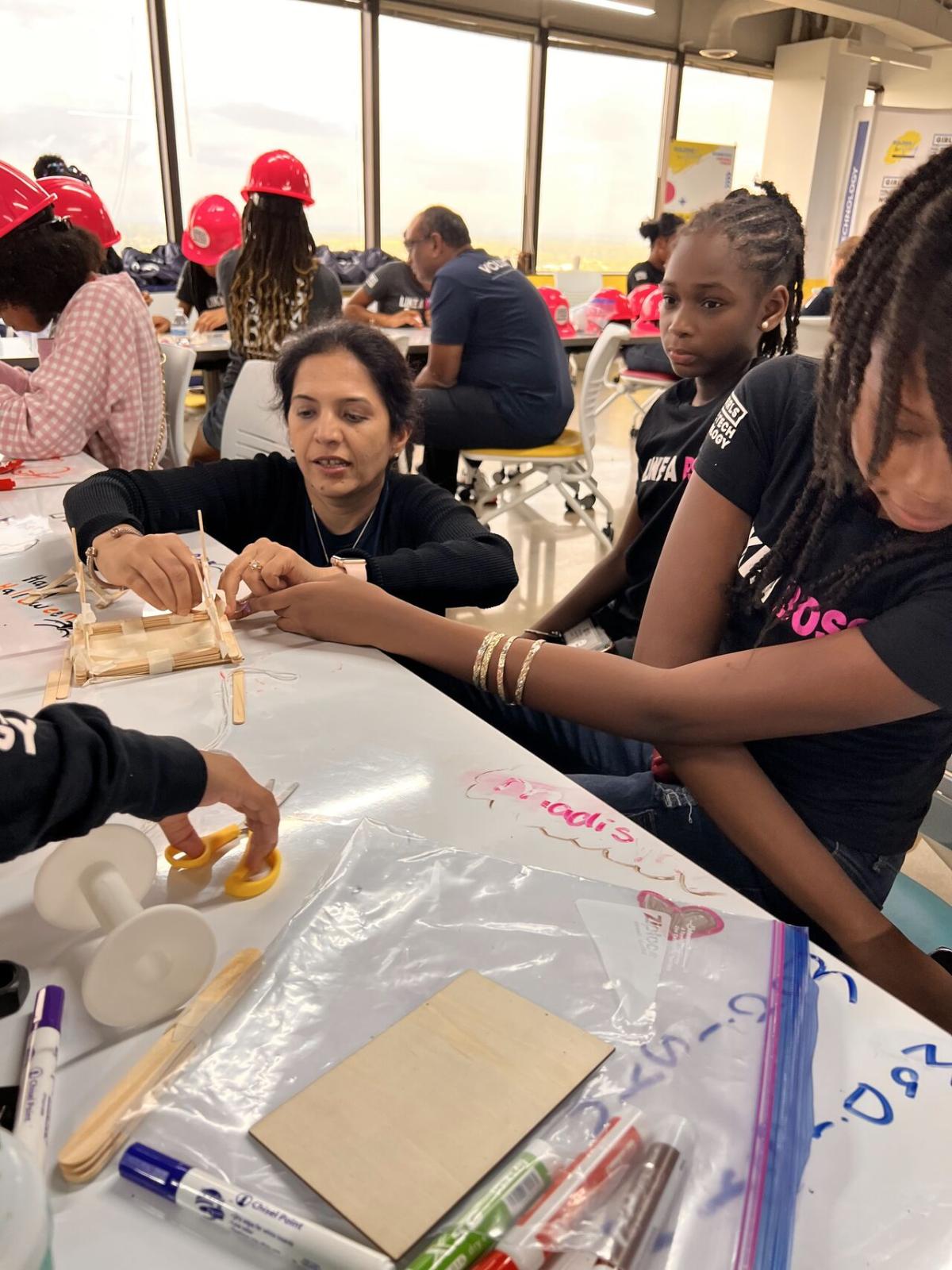 Adult volunteers and children working on building model structures with craft supplies.