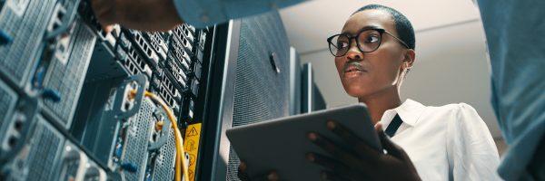 A person holding a tablet, looking at towers of electronic equipment.