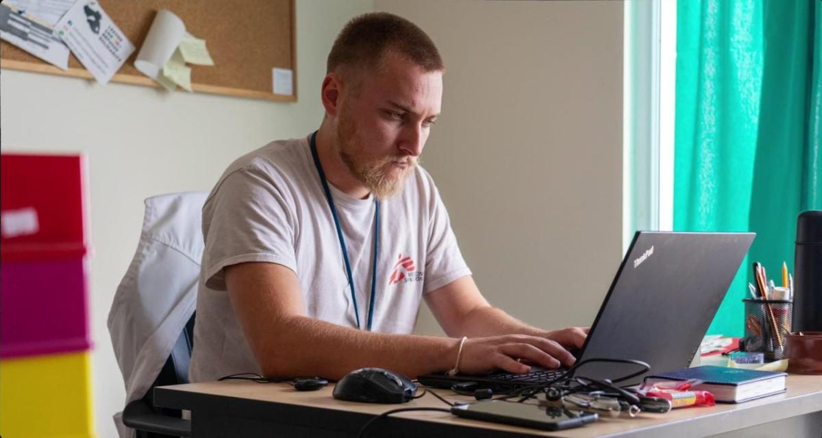 A person seated, working on a laptop in an office setting.