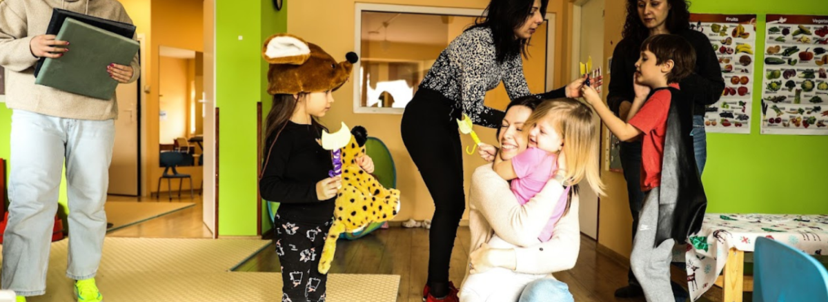 Children and adults smiling and gathering together in a lime green room, one child has a stuffed tiger.