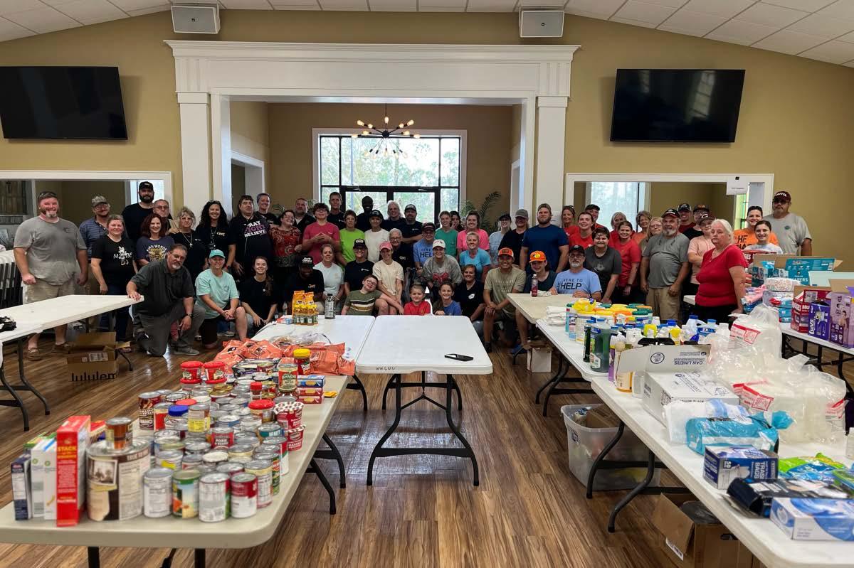 A large group of people posed behind tables full of canned food items and supplies.