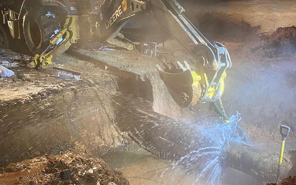 a backhoe poised over a burst water pipe