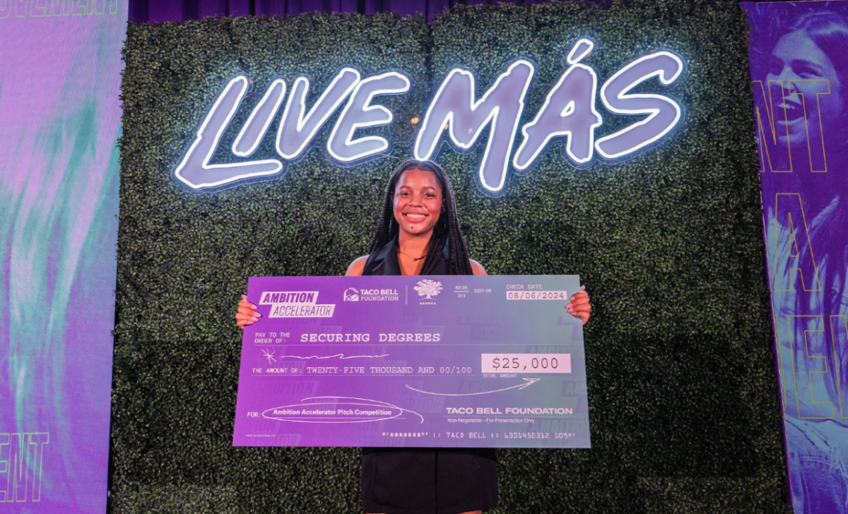 A person holding an oversized check in front of a wall that says "Live Mas"