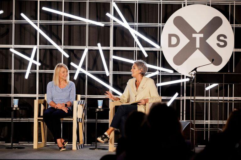 Two people seated on a stage. DTS logo displayed behind them.