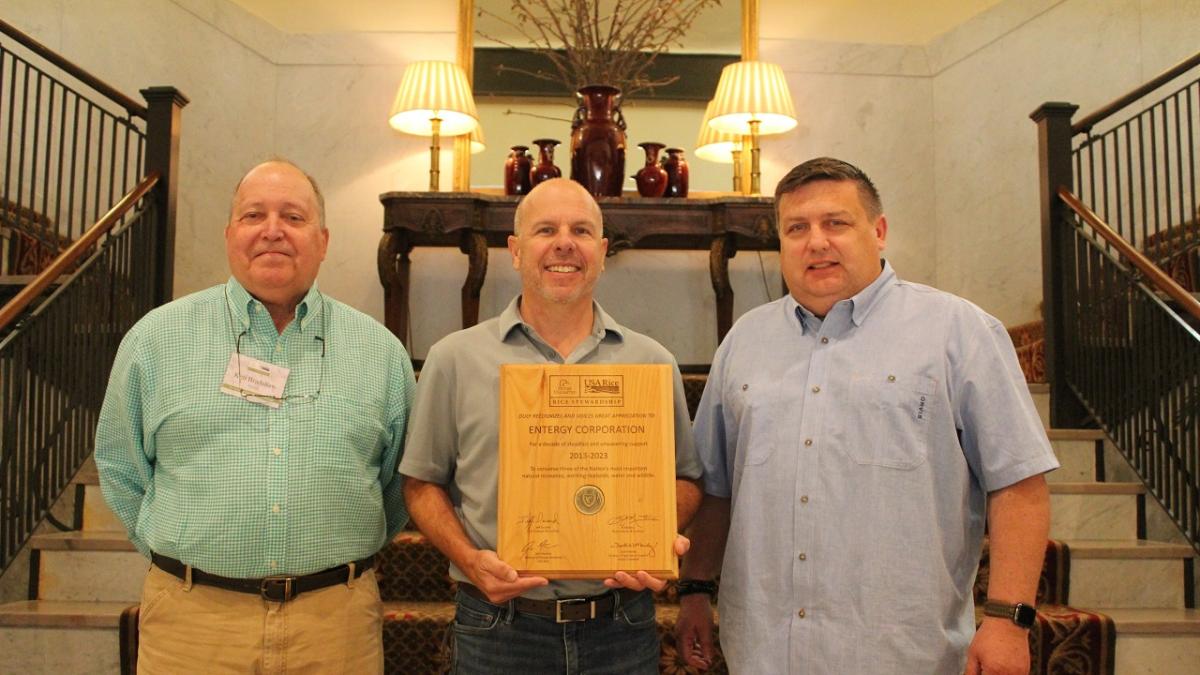 Three people on a staircase, one holds a plaque