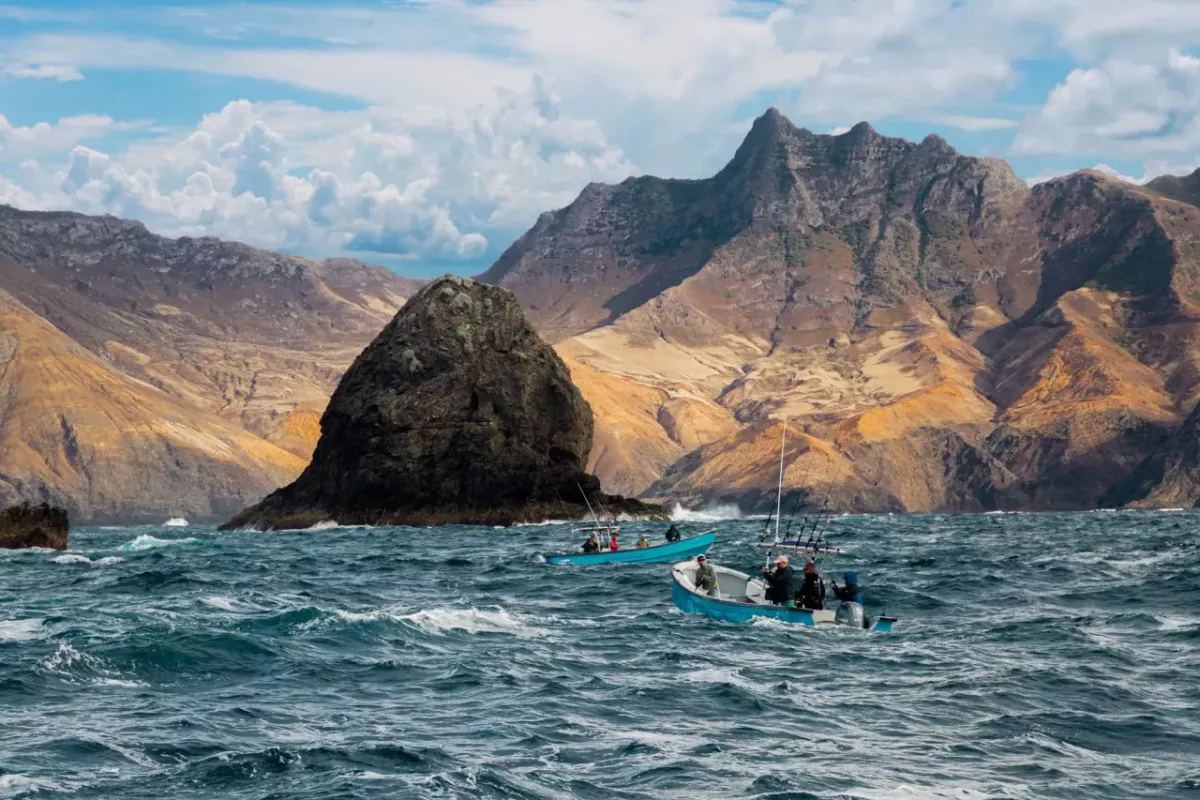 Boats in a large body of water, a mountainous terrain just behind them.