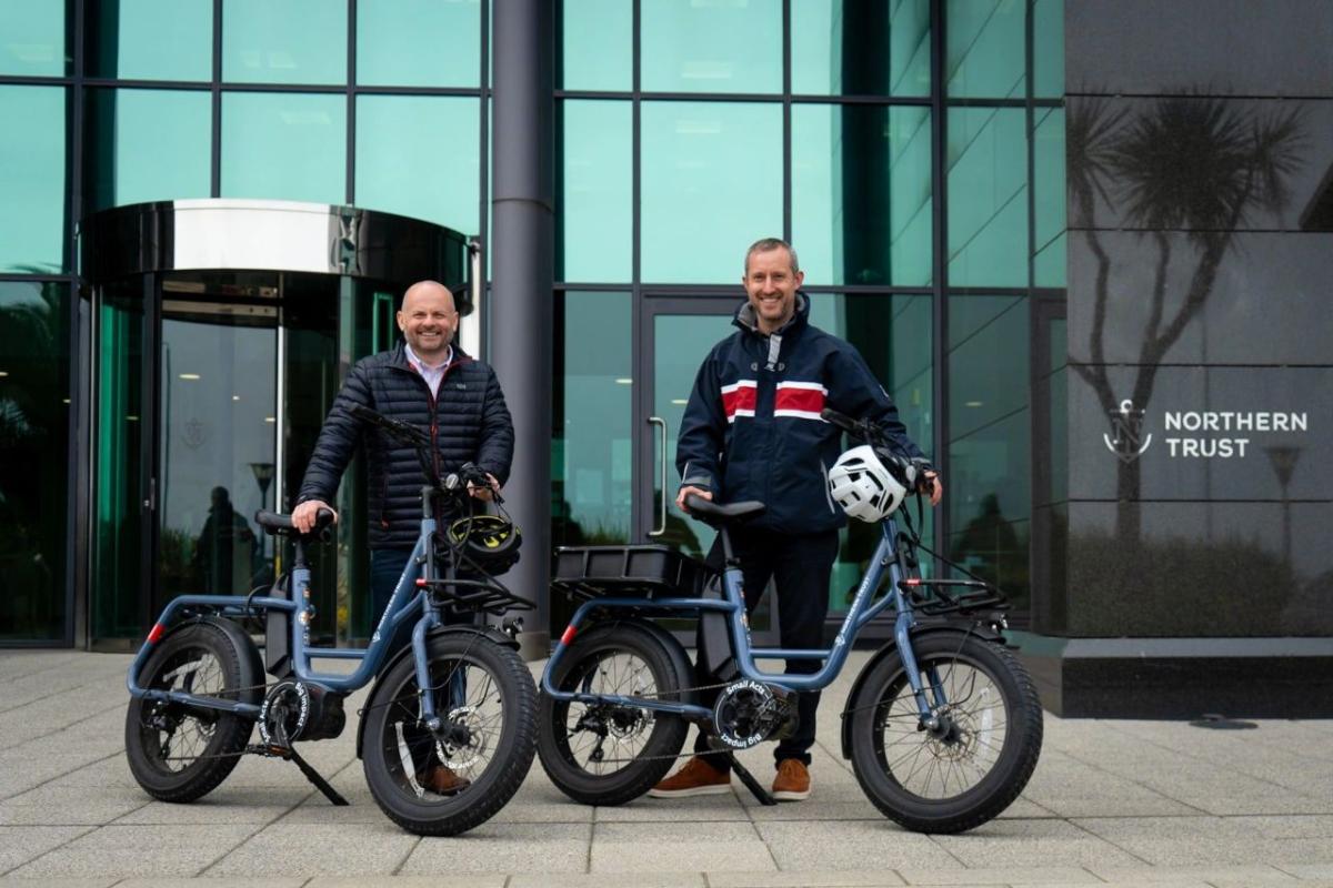 Pete Bowker and Daniel Usher posed by e-bikes outside a Northern Trust building.