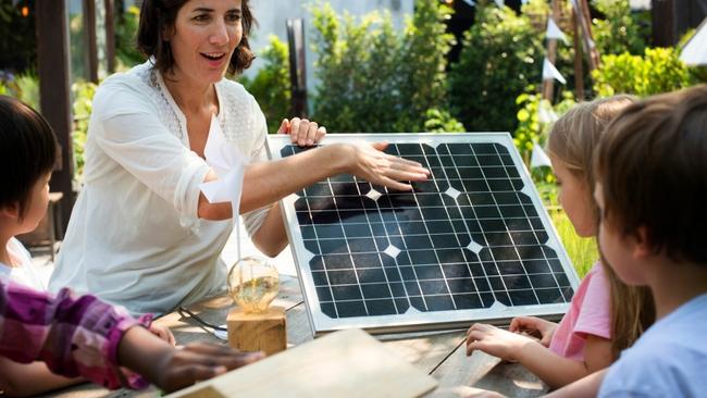 An adult showing children a small solar panel in an outdoor setting.