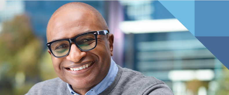 A person smiling, wearing black rimmed glasses. Blurred background.