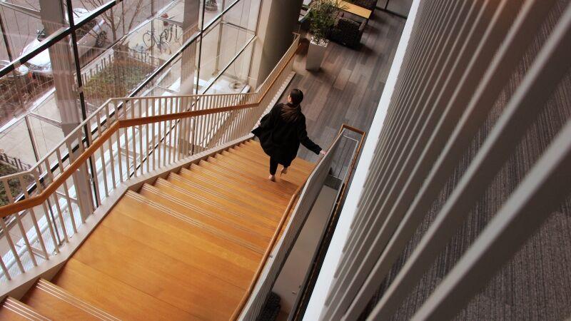 A person walking down a long, wooden, staircase.