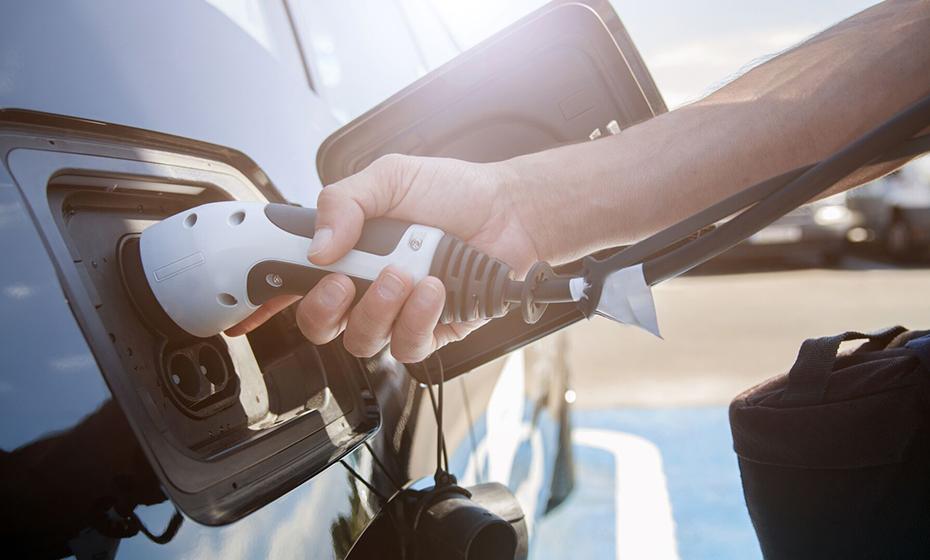 A hand holding a plug to an electric vehicle.