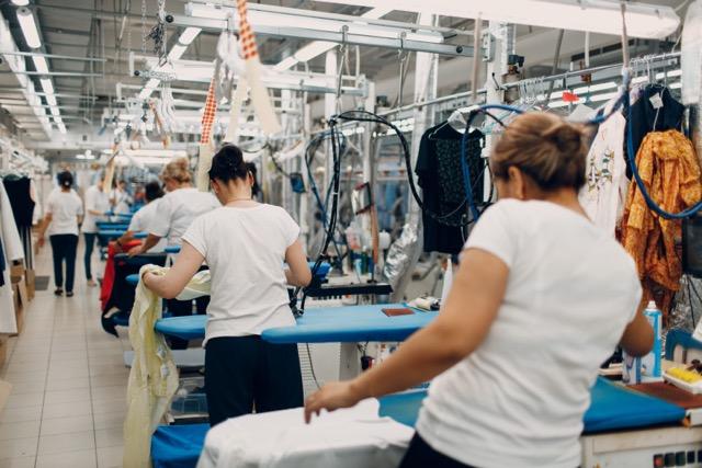 Line of workers standing by irons at garment factory