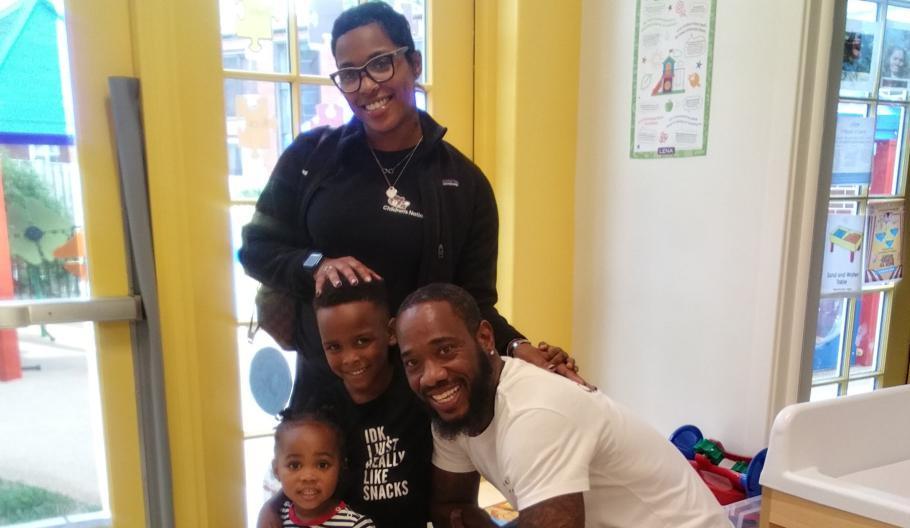 A smiling family posed in a classroom.