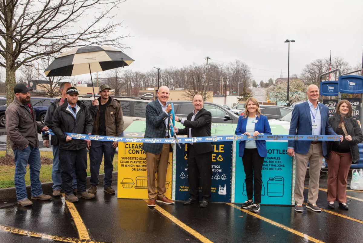 People standing in a parking lot in the rain during a ribbon cutting ceremony