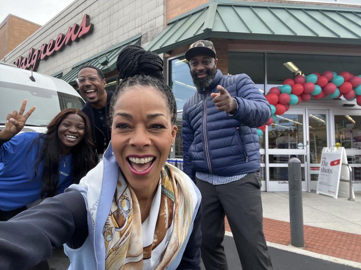 Four smiling people taking a 'selfie' outside a Walgreens.