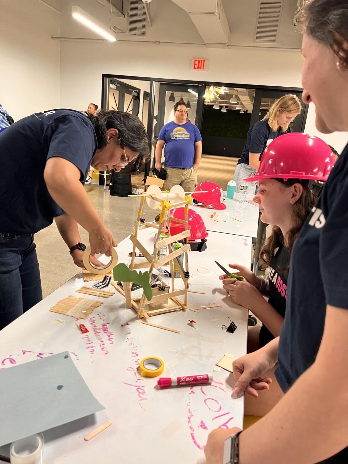 Adult volunteers and children working on building model structures with craft supplies.