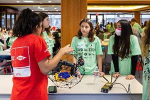 students working on a robotics project in a large room with others