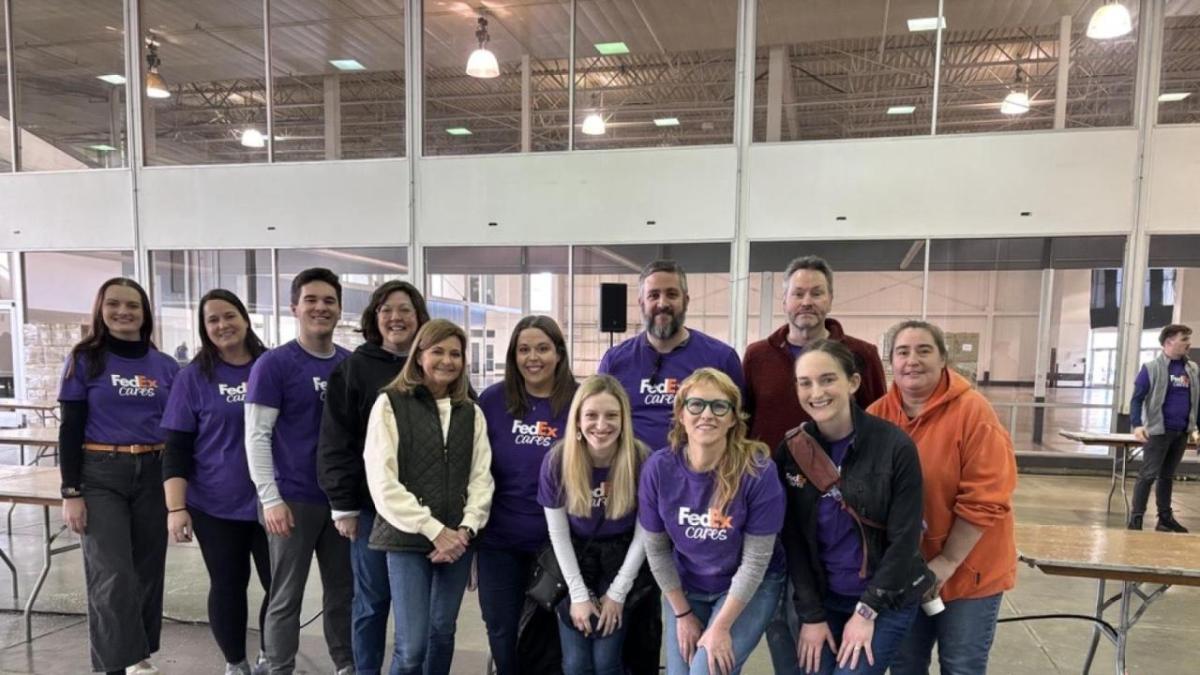 A group of people in FedEx Cares t-shirts posing inside a building