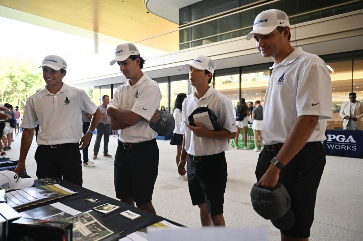 Four standing people in matching clothes look at a booth with materials on it.