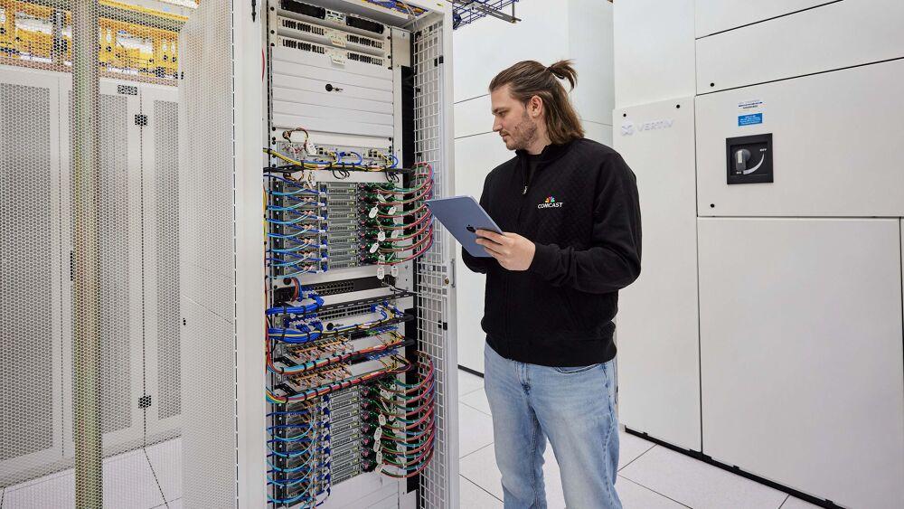 A person with an electronic device looking at a tall box with many wires and computer parts.