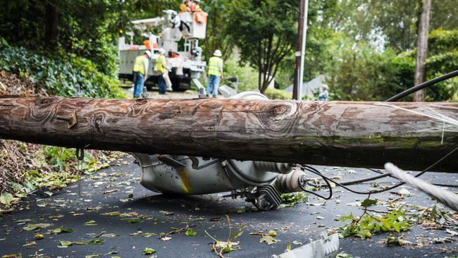 Fallen telephone pole with workers in the background