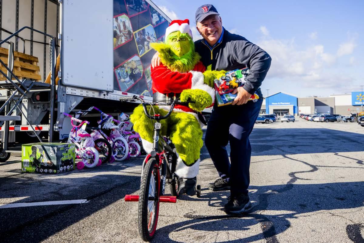 A person dressed as the Grinch on a bicycle, hugging a volunteer.