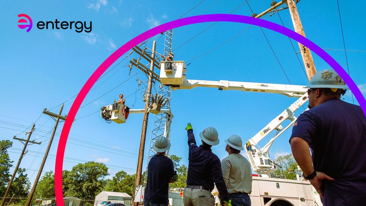 Four people in hard hats looking up at two in lift trucks working on power lines.