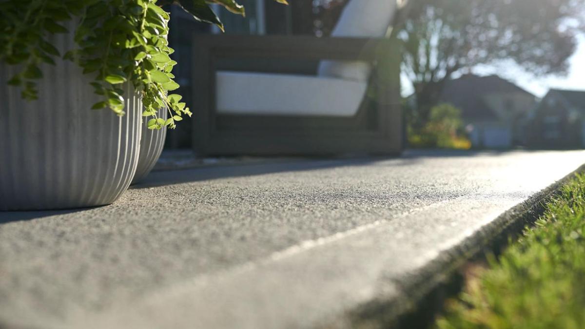 Close up of a paved area next to grass. A chair and potted plant in the background.