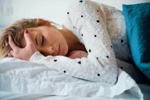 A person lying in a bed, holding their head.