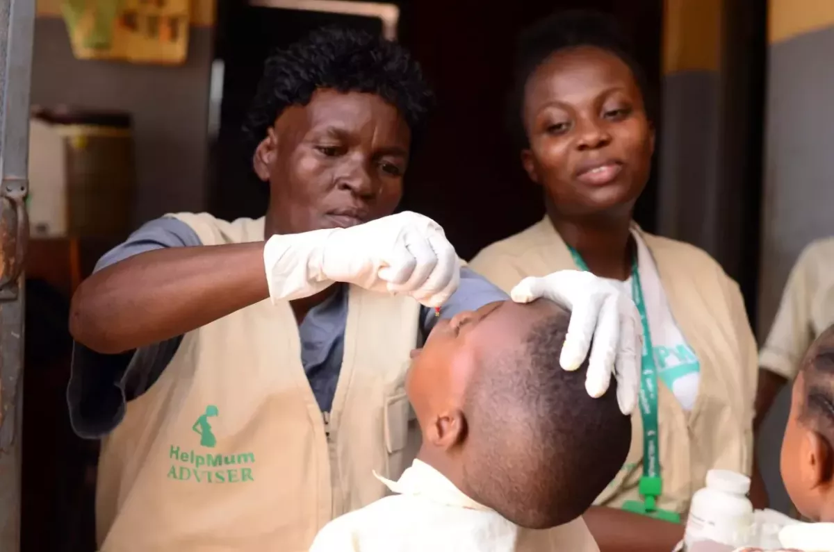 A healthcare worker giving drops to a child as another watches.