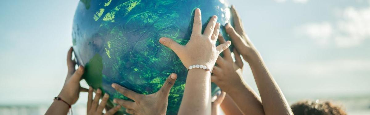 Many children's hands holding up a colorful ball.