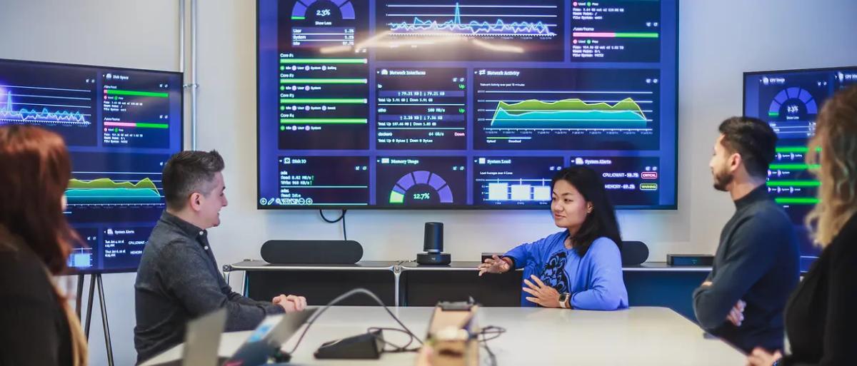 People meeting and looking at multiple screens on a wall.