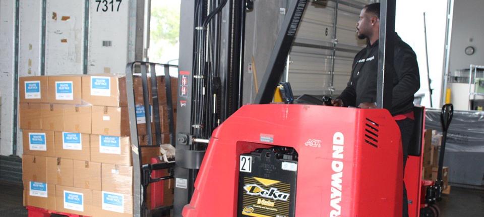 A person driving a forklift loaded with boxes.