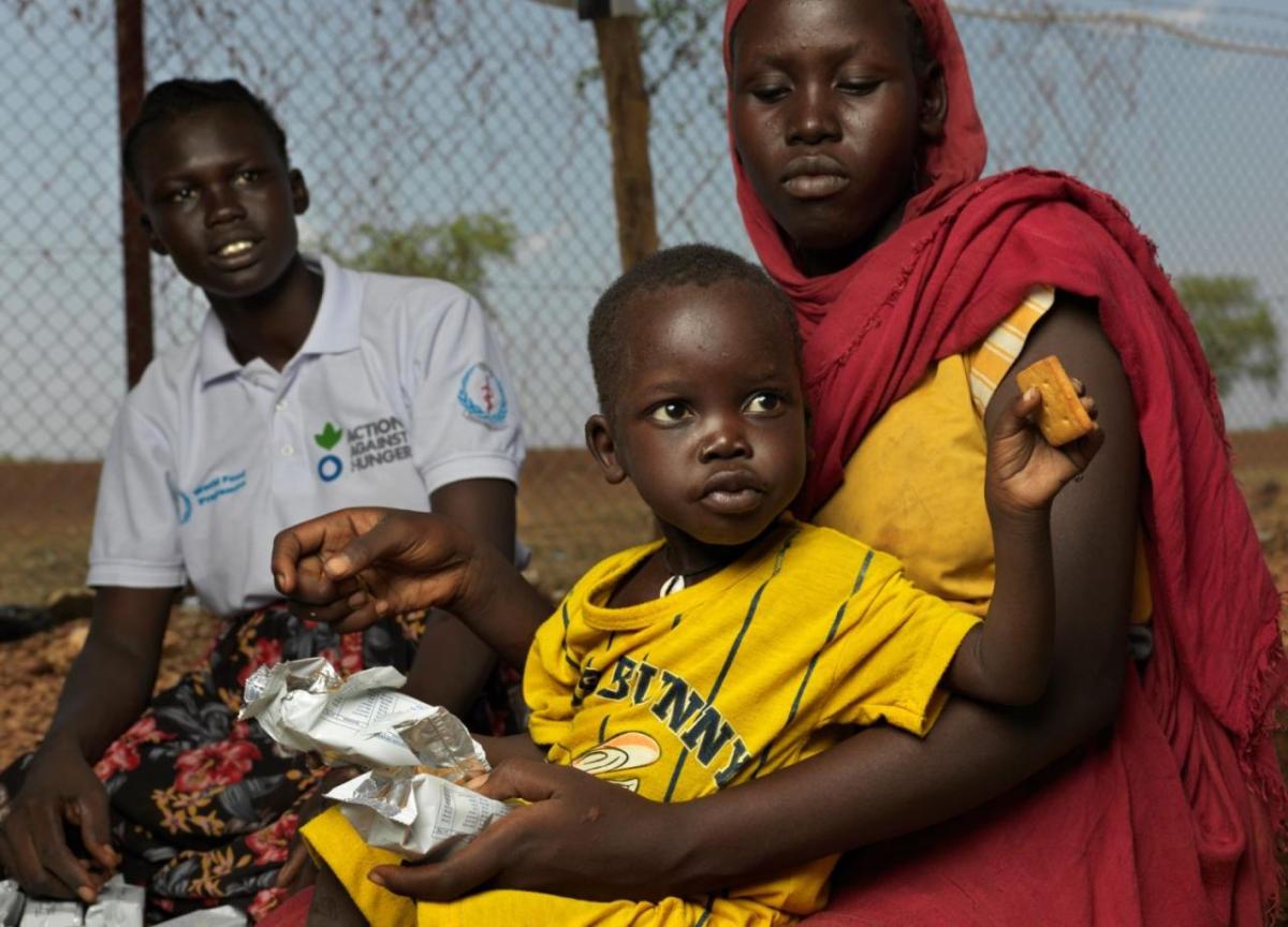 Pregnant Adheet Akeen Alhia, 20, and her child receive energy biscuits from Mary Anok Juac who works for Action Against Hunger.