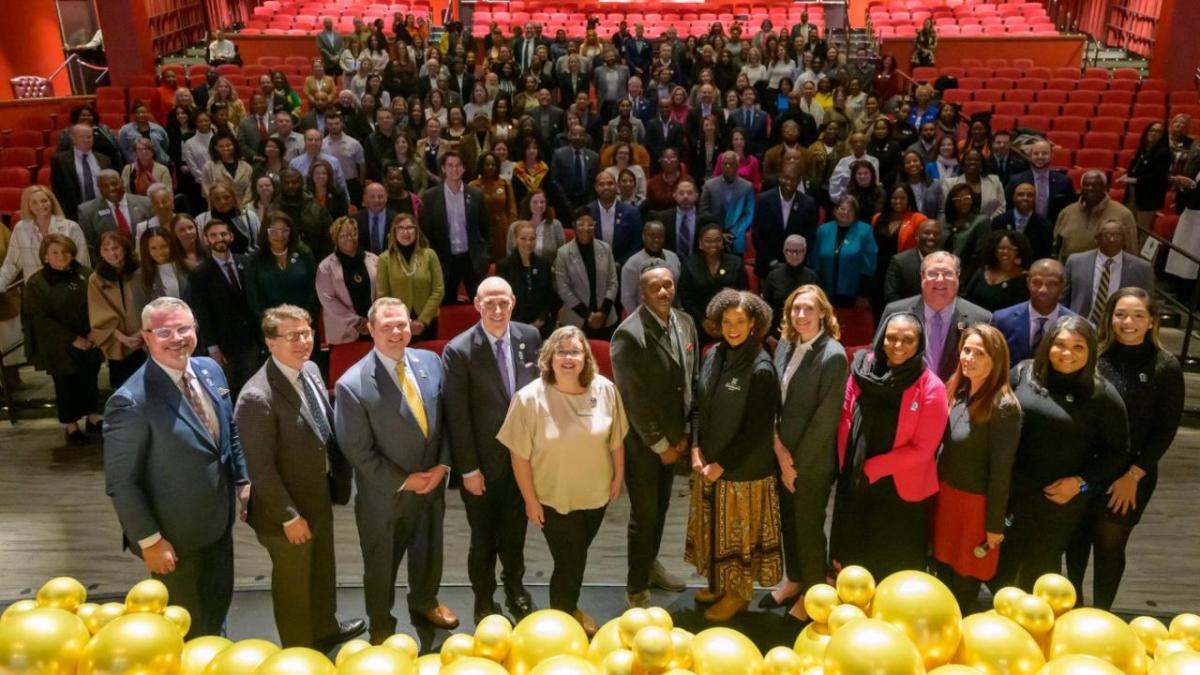 A large group of people posed on a stage and in the seating area.