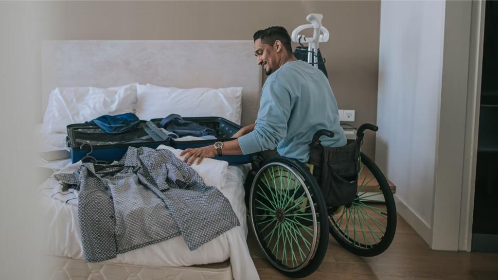 A person in a wheelchair packing clothes into a suitcase on the bed