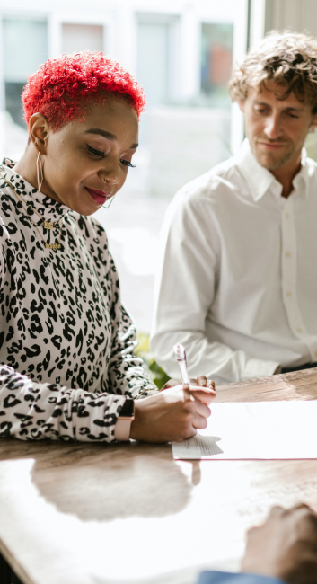 two people at a table, one writing on a piece of paper