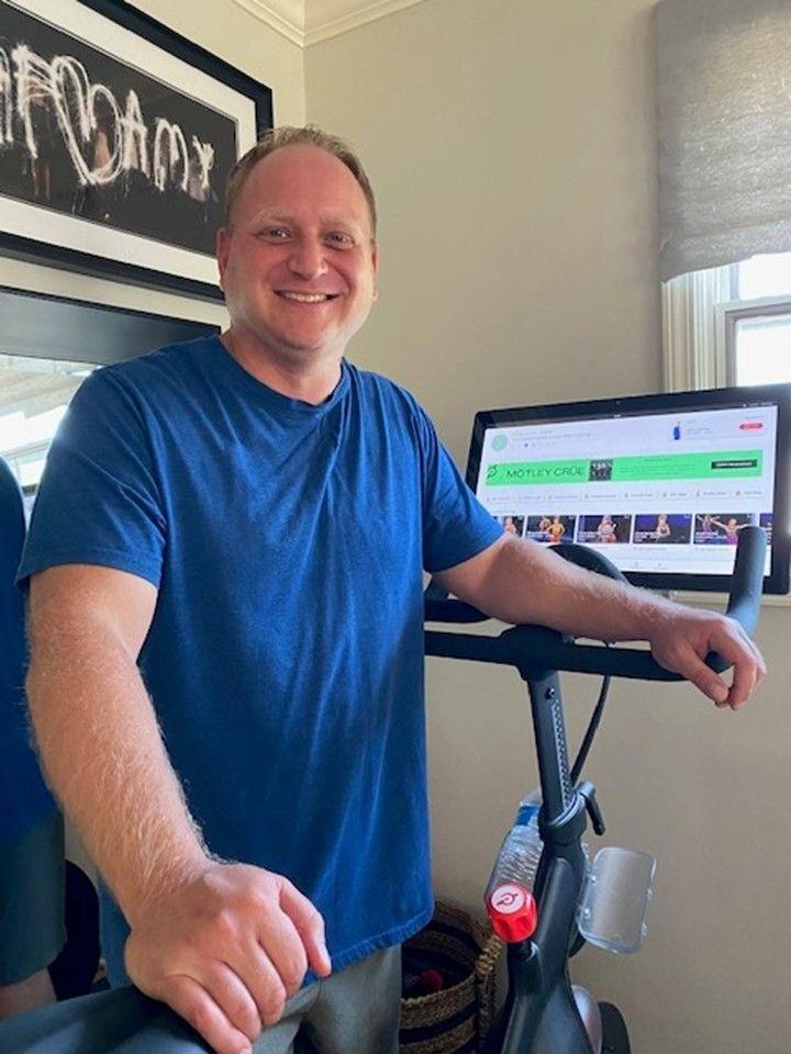 A person smiling next to an indoor bike. 