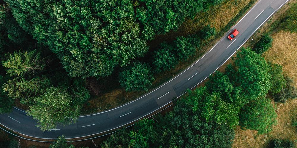 Aerial view of a single red car on a two-way road through forested area