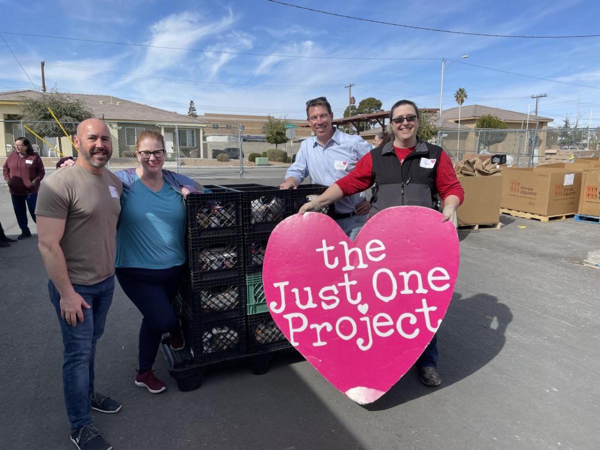 Four posed outside by a stack of milk crates. One holds a sign "the Just One project."