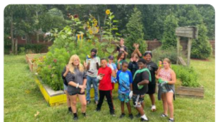 Kids and adults, some with raised hands, posed outside in front of a garden.