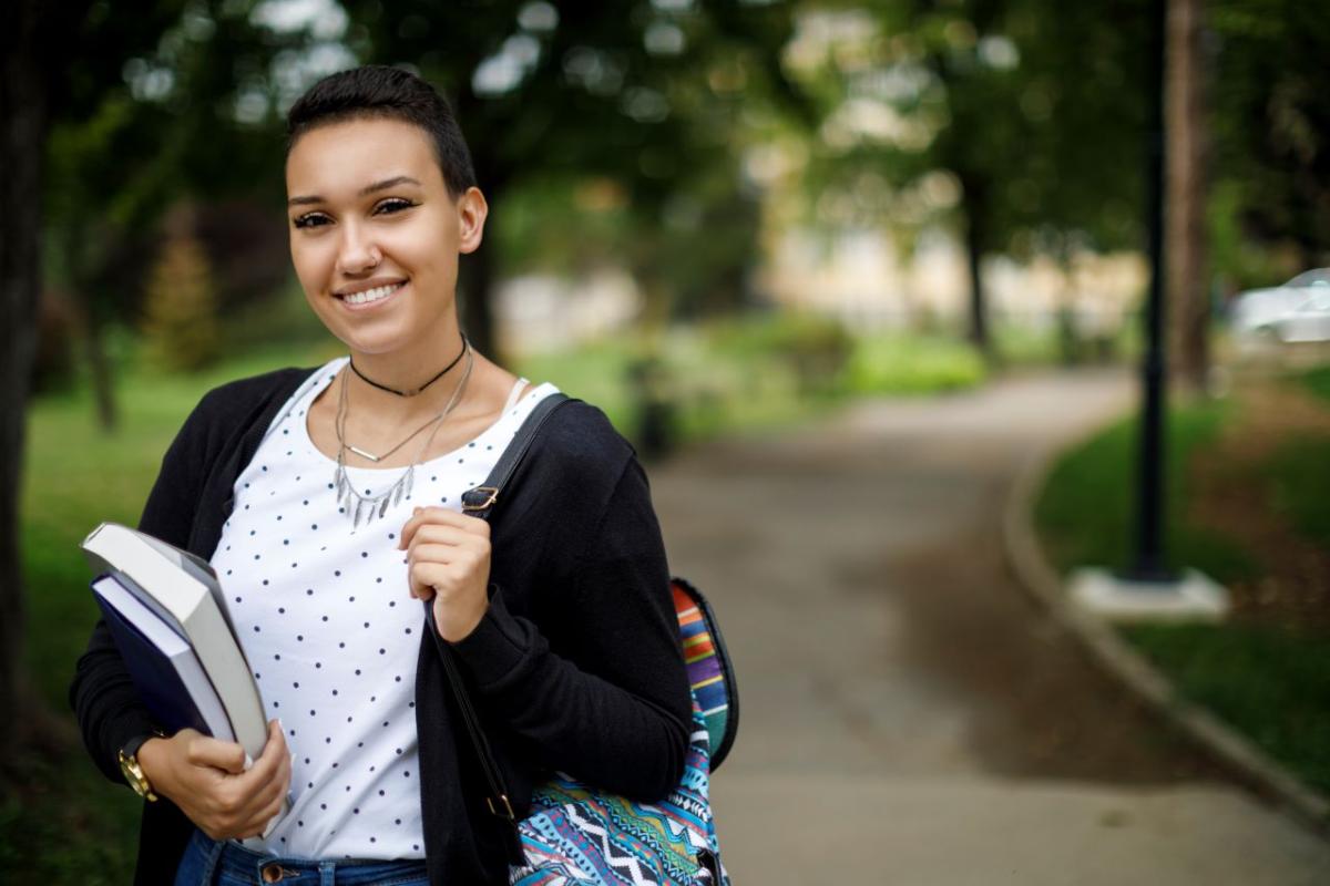 A smiling person with backpack and books.