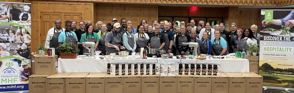 A large group of people posed behind a counter with kitchen appliances on it.