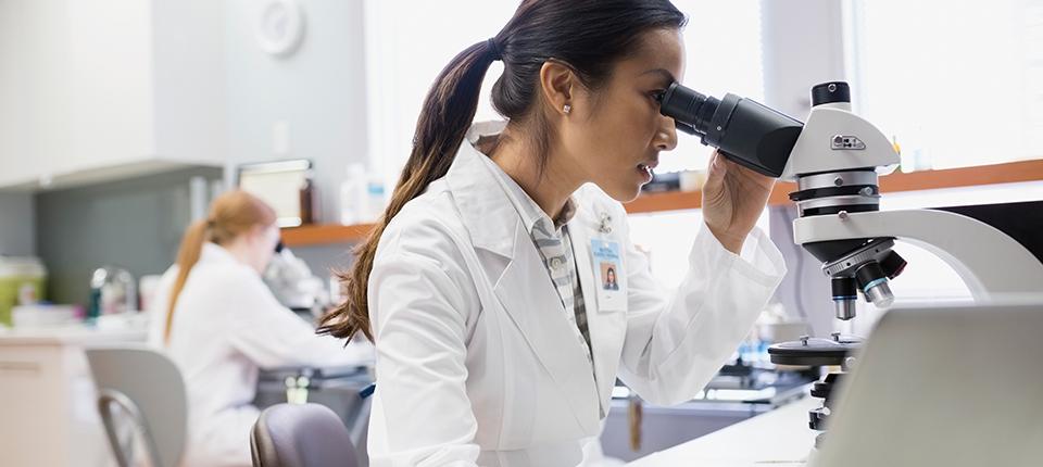 A person in white lab coat looking in a microscope