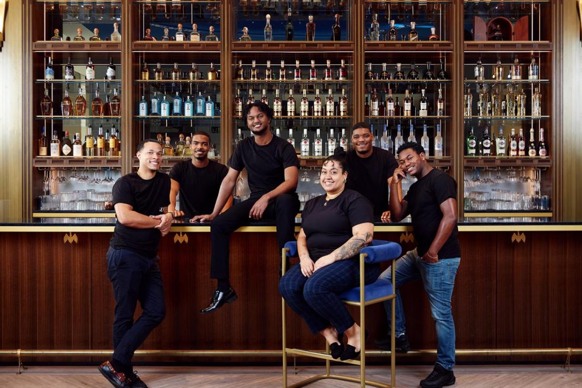 A group of students in black t-shirts posed in front of a bar