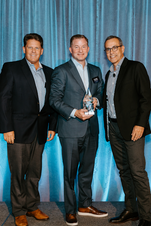 Three people stood next to each other holding an award, in front of a blue backdrop  