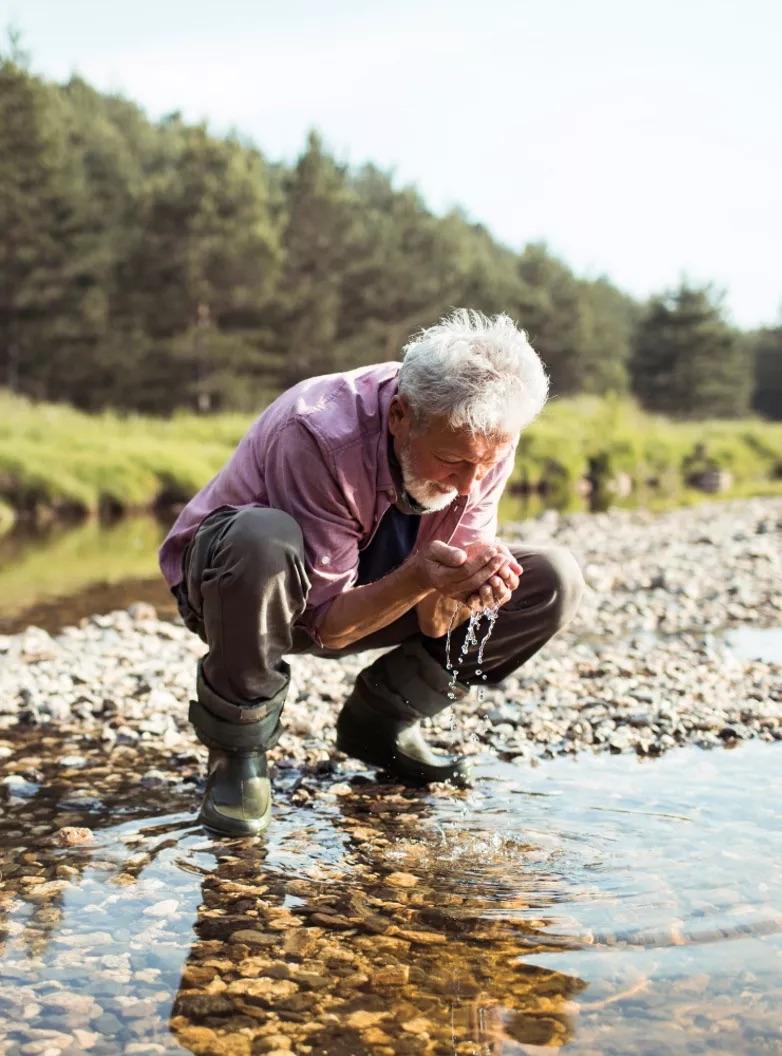 A person crouched down at the side of a river 