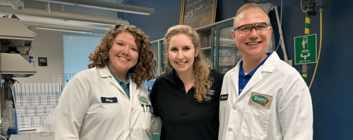 Three people posed together, two in lab protective wear.